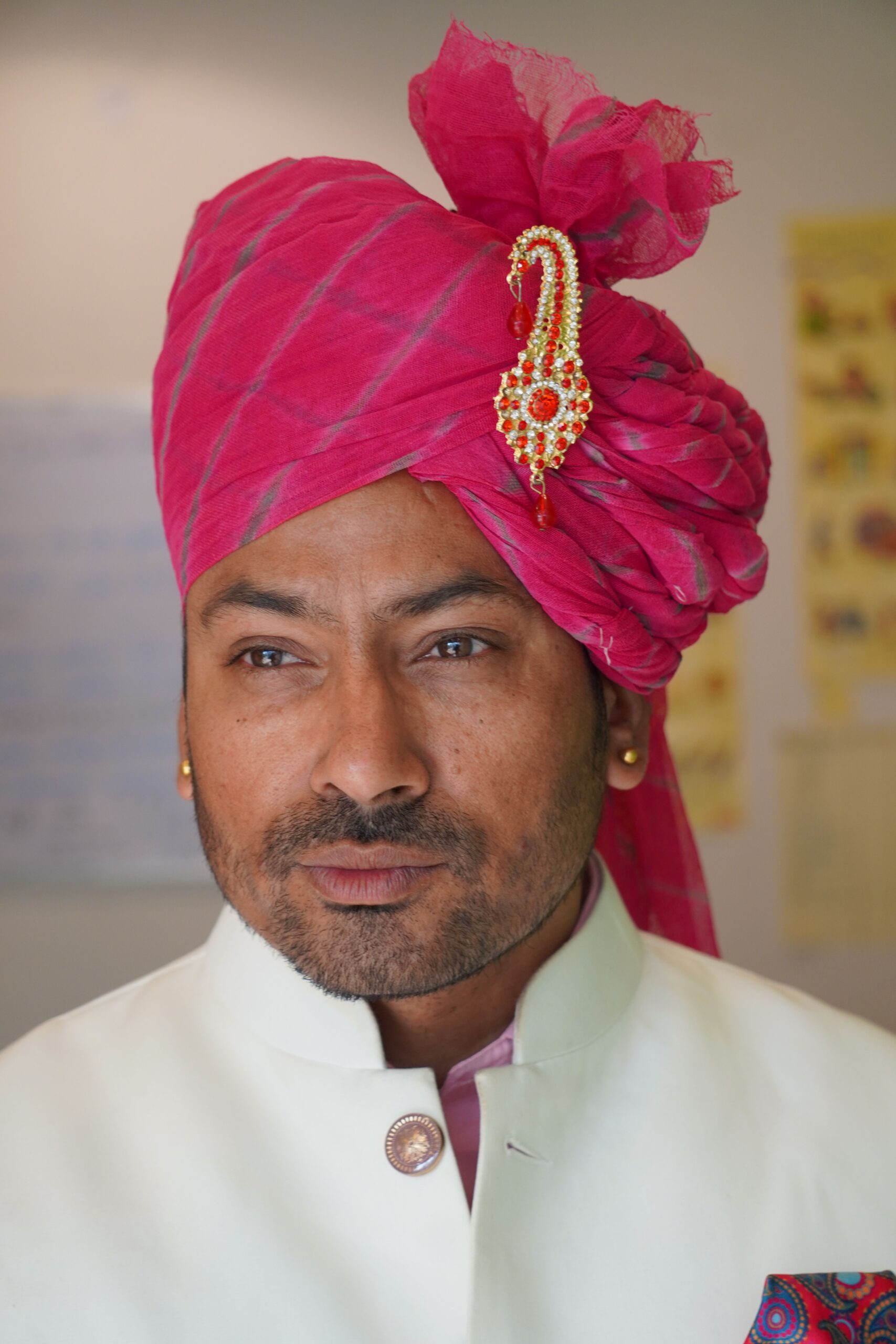 Portrait of an Indian man wearing a vibrant pink turban and traditional Indian attire indoors.